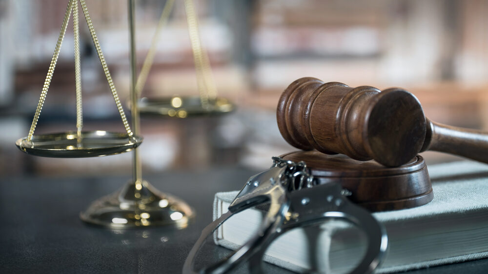 Scales of justice and gavel on a legal book with handcuffs, symbolizing criminal defense and assault law in Texas.
